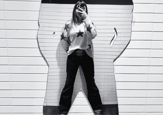 Image of young woman taking picture of self in mirror shaped like a large cowboy_ Mirror poem by Dawn Francis_Rebel-Faith_2024